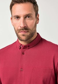 Rode kortärmelige shirt met een button-down kraag, voorzien van een klein geometrisch patroon en een borstzak. De stof lijkt textuur te hebben.