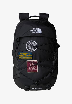 Mochila preta com vários patches, apresentando um logótipo, design de cordão elástico e uma textura suave. Inclui alças e fecho com zíper.