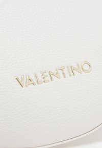 Weiße Leder-Clutch mit strukturierter Oberfläche und goldfarbener, geprägter "VALENTINO"-Logo. Runde Form mit sauberen Kanten.