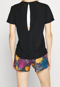 Black mesh short-sleeve top with a keyhole back detail; worn over floral-patterned shorts featuring yellow, purple, and teal roses.