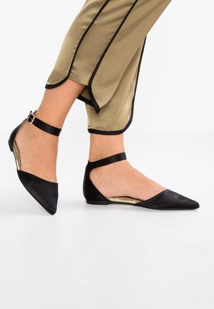Zwarte platte schoenen met een puntige neus, gemaakt van satijn. Voorzien van een enkelbandje met een gesp en een lage hak. Gouden accenten aan de binnenkant.