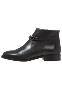 Botín negro de cuero con una superficie suave, tacón bajo y un adorno de cadena alrededor del tobillo. Diseño simple sin patrones visibles.
