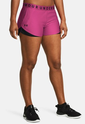 Pantalones cortos deportivos rosas con acentos negros y logo de Under Armour en la cinturilla. Textura suave, diseño ajustado. Zapatillas deportivas negras con suela blanca.