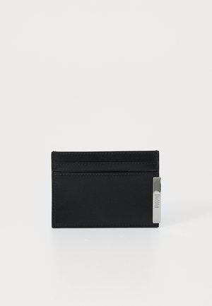 Cartão de couro preto com uma textura suave, vários slots para cartões e um detalhe em metal prateado de um lado. Design minimalista, forma retangular.