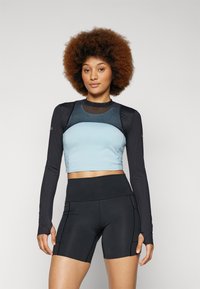 Crop top in light blue with black long sleeves, smooth fabric, rounded neckline; paired with high-waisted black shorts featuring seams.