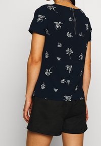 Haut bleu marine à manches courtes, avec un motif floral blanc et une fermeture éclair dans le dos. Associé à un short noir en tissu respirant.