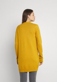 Cárdigan amarillo de punto con un diseño largo, puños y dobladillo acanalados, mostrado desde la parte trasera contra un fondo neutro.