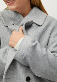 Szary wełniany płaszcz z dużym kołnierzem, fakturowaną tkaniną i podwójnym zapięciem na guziki. Na rękawie ozdobny kremowy mankiet.