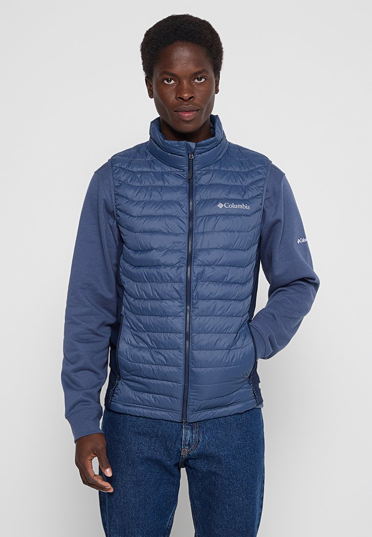 Gilet blu navy con frontale quilted, col alto e maniche in pile. Presenta chiusura con zip e logo sul petto. I jeans in denim completano l'outfit.