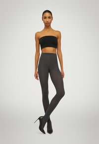 Collant opachi grigio scuro con una vita alta, texture liscia e design aderente. Indossati con scarpe nere con tacco alto e un top bandeau nero.