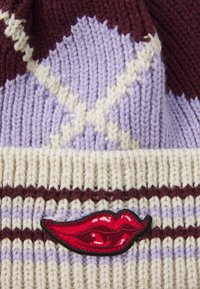 Berretto lavorato a maglia in crema, viola e bordeaux, con un motivo a diamante e un logo labbra ricamato di rosso sul davanti. Tessuto morbido.
