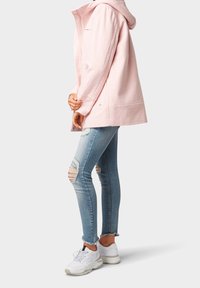 Chaqueta de mezcla de lana color rosa claro con capucha, combinada con jeans skinny deslavados azul claro y zapatillas blancas. Estilo casual, ajuste relajado.