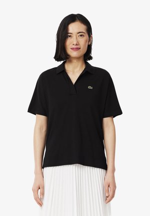 Polo noir à manches courtes, col rabattable et petit logo vert. Fabriqué en tissu lisse, il possède une coupe oversize.