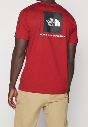 Red cotton t-shirt featuring a black square graphic with "THE NORTH FACE" logo and "NEVER STOP EXPLORING" text on the back.