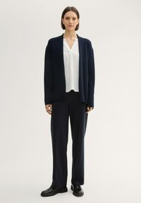 Cardigan marine à ouverture sur le devant, associé à une blouse blanche et un pantalon large marine. Texture lisse ; coupe ajustée ; design minimaliste.