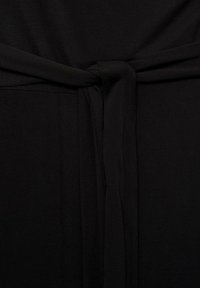 Tissu noir avec une texture lisse, comportant une ceinture nouée au centre. Le design est simple, axé sur l'esthétique monochrome sombre.