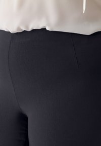 Schwarze Leggings aus glattem, dehnbarem Stoff mit enganliegendem Schnitt und leichtem Glanz. Keine sichtbaren Taschen oder Verzierungen.