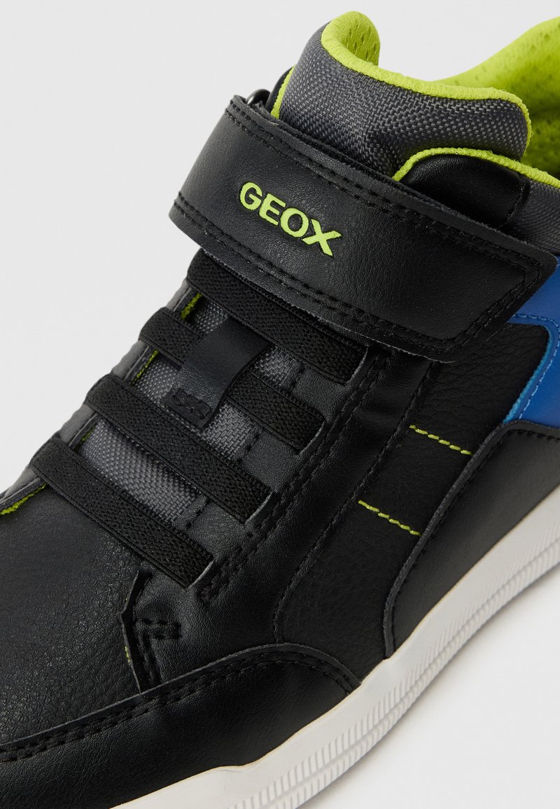 Schwarze Ledersneaker mit grünen Akzenten, elastischen Schnürsenkeln und einem Klettverschluss. Verfügt über ein blaues Seitenteil und eine strukturierte Oberfläche.