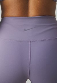 Gros plan sur le bas du dos et la taille d'une personne portant un legging Nike violet taille haute avec des détails de couture visibles.