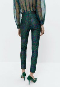 Farkkuhousut, joissa on vihreä kukkakuosi ja korkea vyötärö, kiiltävä pinta, koristeltuna punaisilla ja violetilla kukilla. Yhdistetty vihreisiin korkokenkiin.