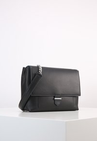 Borsa a tracolla in pelle nera con chiusura a pattina, hardware argentato e tasca frontale. Dotata di una tracolla staccabile. Texture liscia.
