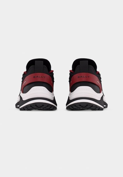 Paire de baskets noires et blanches avec des bridettes rouges au talon portant l'inscription "BALLY", vues de dos sur un fond blanc.