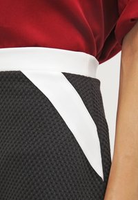 Gonna in tessuto nero con texture, caratterizzata da una ampia fascia bianca in vita con un accento bianco diagonale. Il design è moderno e sartoriale.