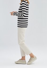 Gestreiftes Langarmshirt in Schwarz und Weiß, kombiniert mit cremefarbenen, geraden Hosen und beigen Sneakers. Leichter Stoff und entspannter Schnitt.