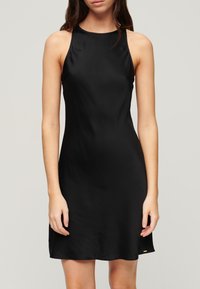 Czarna sukienka bez rękawów o wysokim kołnierzu i gładkiej strukturze, z lekkim kształtem A-linii i małym złotym akcentem przy hemie.