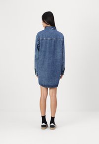 Abito camicia in denim blu chiaro con vestibilitàampia, maniche lunghe e orlo curvo. Caratterizzato da colletto e dettagli sul yoke posteriore.