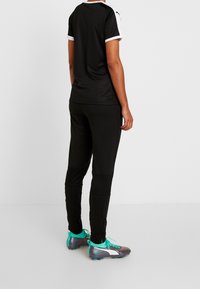 Zwarte sportshirt met witte accenten, gecombineerd met zwarte taps toelopende broeken en grijze sportschoenen met turquoise details. Gladde textuur overal.