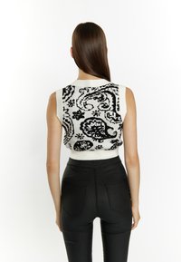 Top tricotat fără mâneci, cu model alb și negru, guler înalt, design ajustat și margini ribbate, asortat cu pantaloni negri cu talie înaltă.