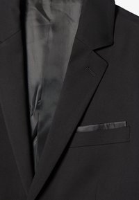 Sacou negru cu o textură netedă, rever înclinat și un singur buzunar pe piept. Interiorul are o căptușeală contrastantă și o cusătură elegantă.