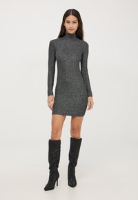 Krótka szara sukienka z wysokim dekoltem, długimi rękawami i dopasowanym krojem, z metalicznym połyskiem. Noszona z czarnymi kozakami do kolan.