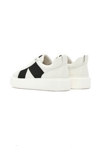 Des baskets en cuir blanc avec un design géométrique noir, un col rembourré et une épaisse semelle en caoutchouc blanc. Style minimaliste avec des accents contrastés.