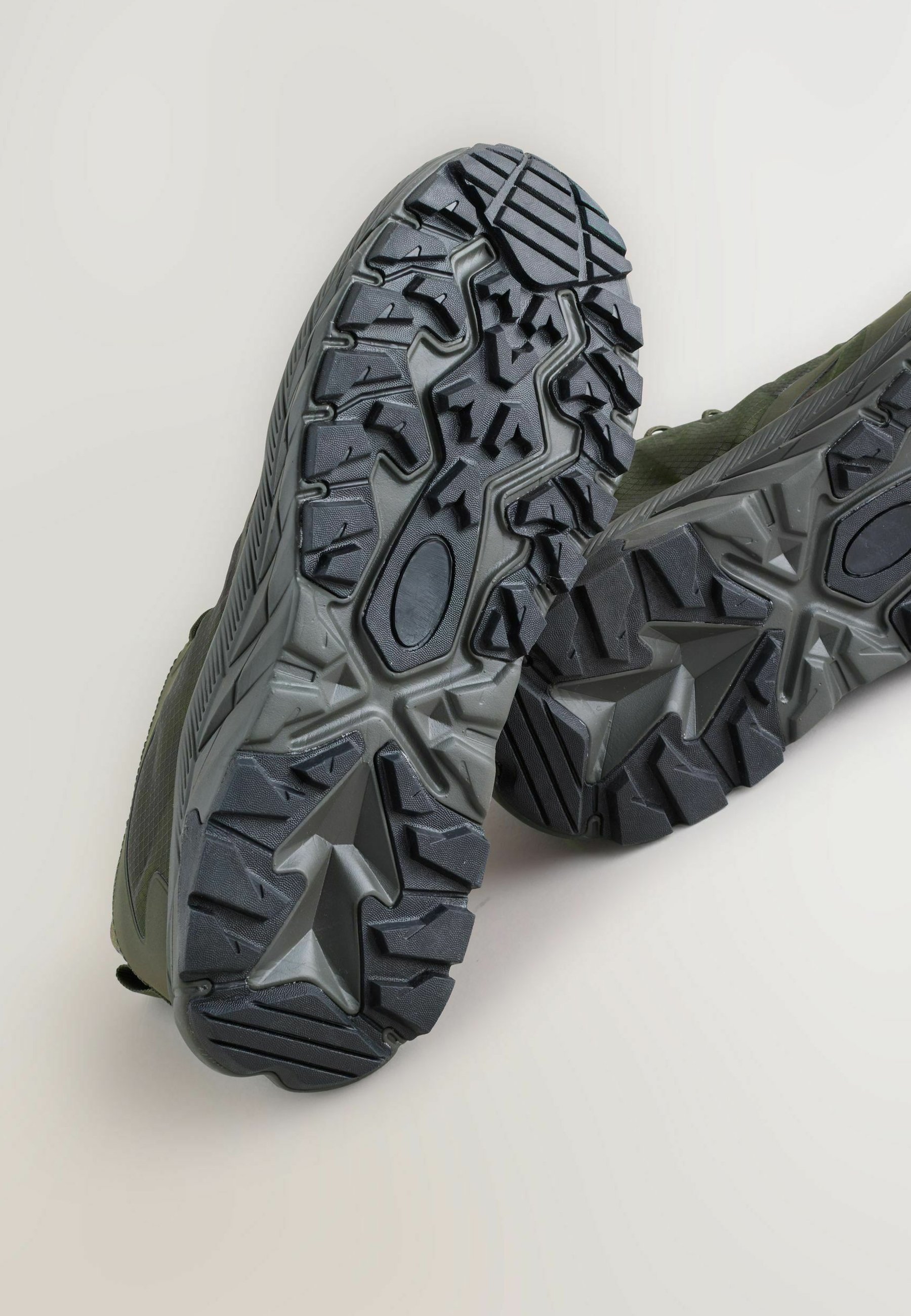 Black rubber shoe soles with a rugged tread pattern. Textured design featuring deep grooves and sharp lugs for enhanced traction.