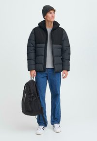 Must must ja hallid voodriga jope, hall sviiter, sinised teksad, must seljakott ja valged tossud, koos tekstuuriga kudumisega beanie'ga.