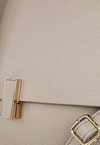 Sac à main en cuir gris clair avec une surface texturée, des accents en matériel doré et un détail de fermeture magnétique rectangulaire.