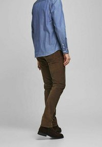 Pantaloni in velluto a coste marroni con una vestibilità slim, abbinati a una camicia di jeans azzurro chiaro, indossati con stivali alla caviglia in suede marrone scuro.