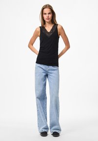 Black sleeveless top with lace V-neckline paired with light blue flared jeans and black shoes. The top has a smooth texture.