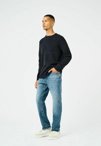 Maglione a coste blu navy, jeans con lavanderia azzurra chiara e sneakers bianche. Il maglione ha maniche lunghe e scollo rotondo, vestibilità casual.