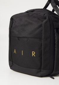 Melna mugursoma ar teksturētu audumu, ar zelta "AIR" logo un priekšējo kabatu. Iekļauta rāvējslēdzēja aizdare un regulējamas siksnas.