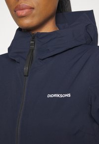 Mörkblå jacka med zippered fram, justerbar huva och vitt "DIDRIKSONS"-logotyp. Har en slät, strukturerad tyg.