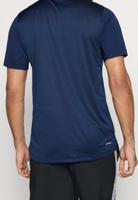 Mörkblå atletisk t-shirt med korta ärmar, tillverkad av lättviktig tyg; har rund hals och subtil textur, med varumärkeslogotyp i fållen.