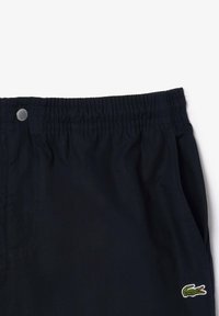 Pantaloni corti blu navy con cintura elastica, dotati di un bottone a pressione in metallo e tasche laterali. Include un piccolo logo di coccodrillo ricamato.