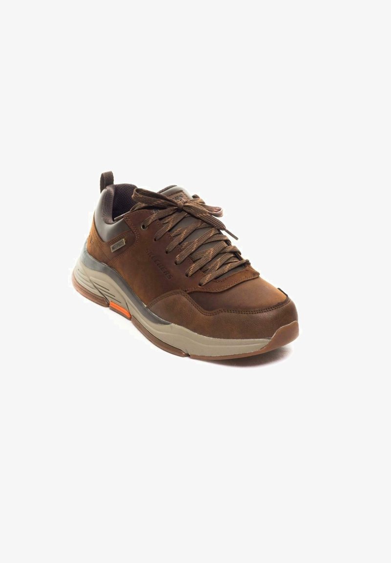 Pruun spordijalanõud, millel on nahast ja sünteetilisest materjalist pealispind, paeltega disain, hall aktsent ja tekstureeritud talla oranž detail.