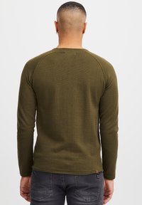 Olijfgroene long sleeve shirt met een gestructureerde brei, raglanmouwen en een gebogen zoom. Bevat een klein logotagje nabij de onderkant rechts.