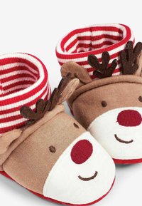 Chaussons doux marron et blanc avec des poignets rayés rouges et blancs. Présente un design de visage de renne, avec des cornes brunes et un détail de nez rouge.