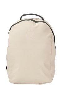 Mochila de color beige claro con una textura suave y mate, forma redondeada, acentos negros en contraste y un logo estampado en la parte delantera.