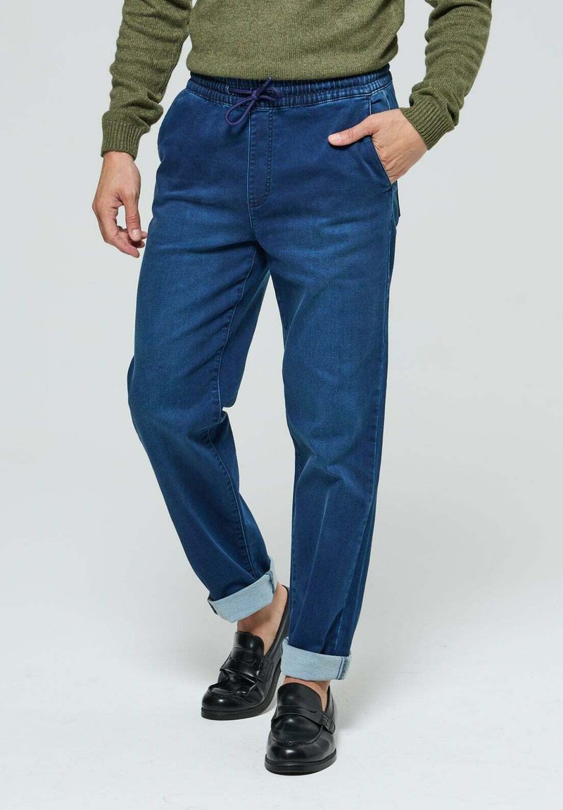 Jogging en denim bleu foncé avec une taille élastique et un cordon de serrage violet. Comprend deux poches latérales et des poignets retroussés.